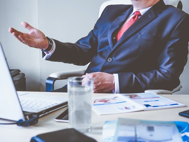 person in suit at a desk in front of a laptop